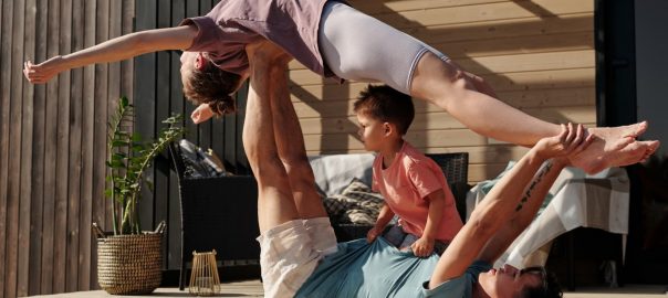 Father and kids doing yoga outdoors on a patio, balancing poses together.